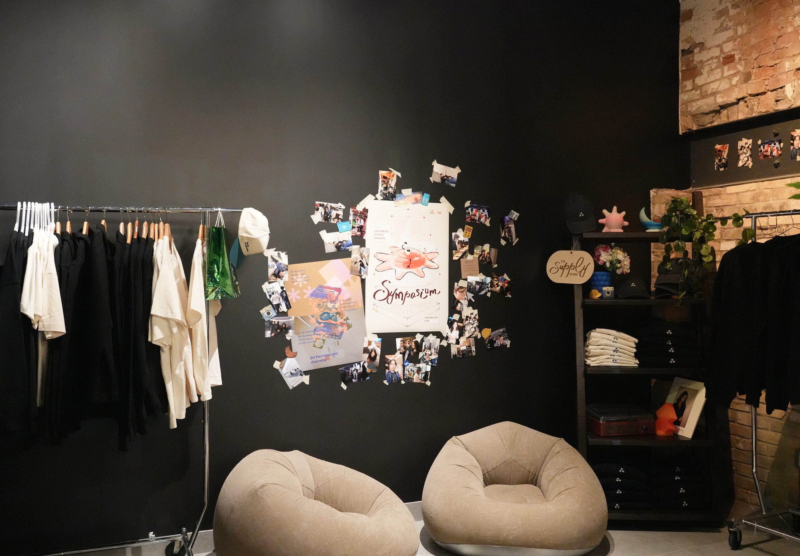 A dark pop-up shop corner with a clothing rack, prints pinned to the wall, and two beanbags.