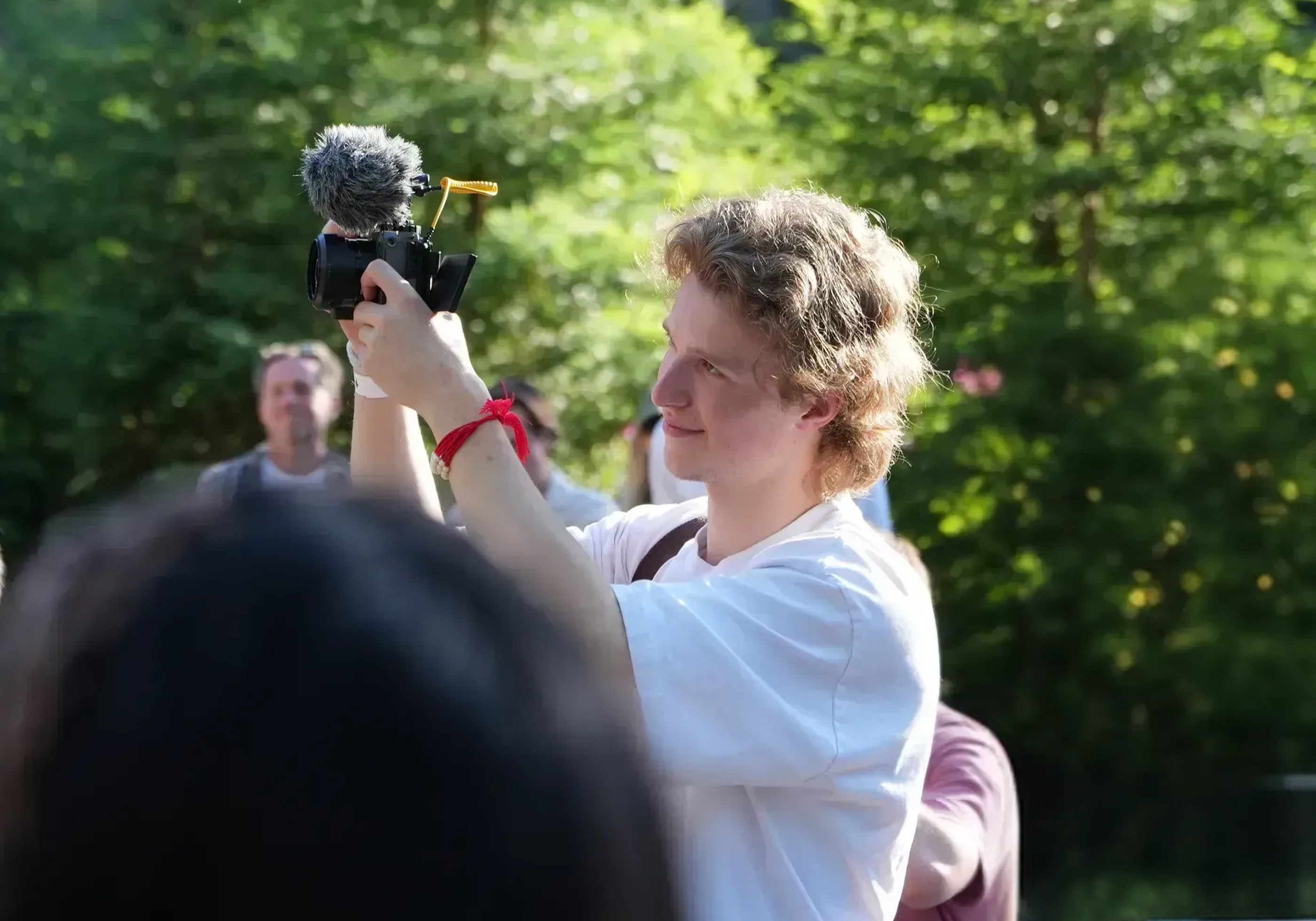 A person filming with a camera and microphone in a crowd.